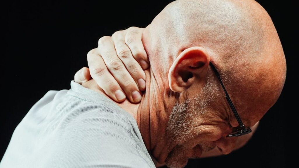 Homem careca, usando óculos, com a mão no pescoço e feição de dor, representando oa rtigo sobre quiropraxia e o alívio das dores